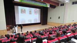 image of a presentation being given on stage to a full lecture hall