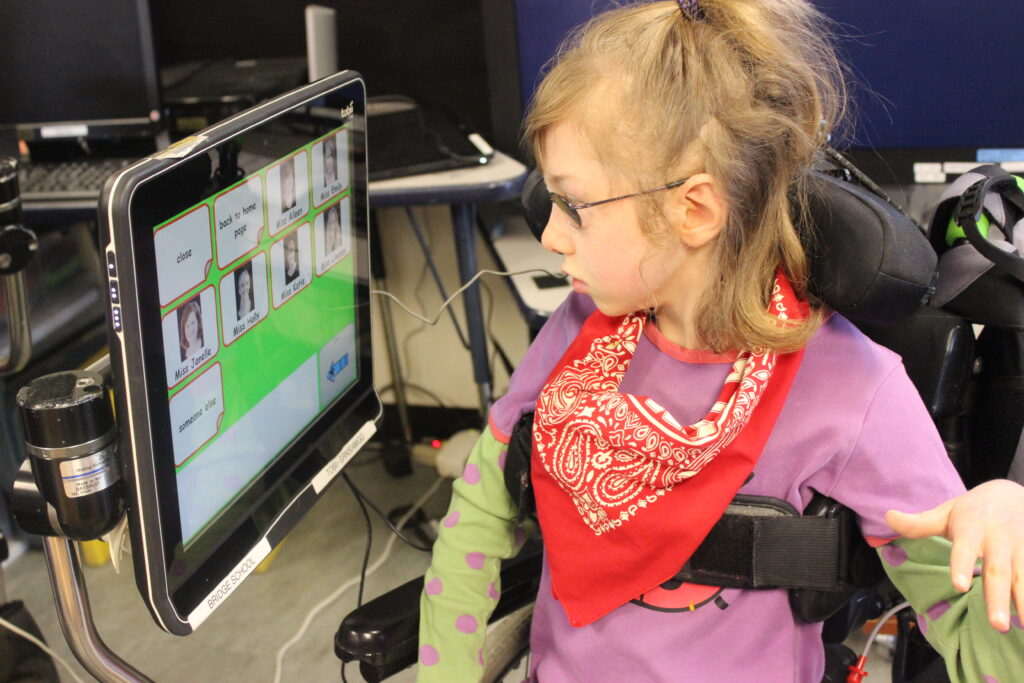 An image of a child in a wheelchair looking sideways at an AAC device