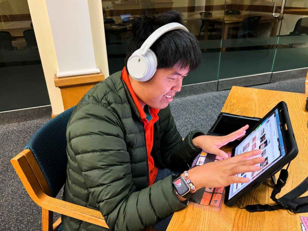 A young man wearing headphones sitting at a table interacting with a digital tablet